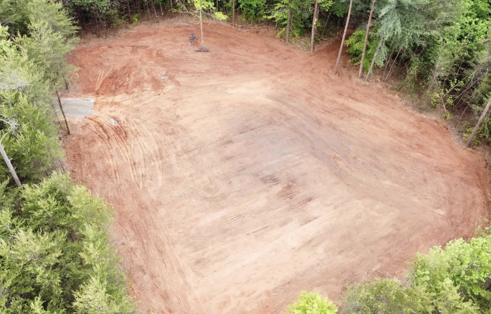 Aerial view of a graded red-clay building pad carved out of the trees